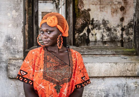 Africa Woman in orange suit and headdress stands by an old building in Takoradi Ghana West Africa